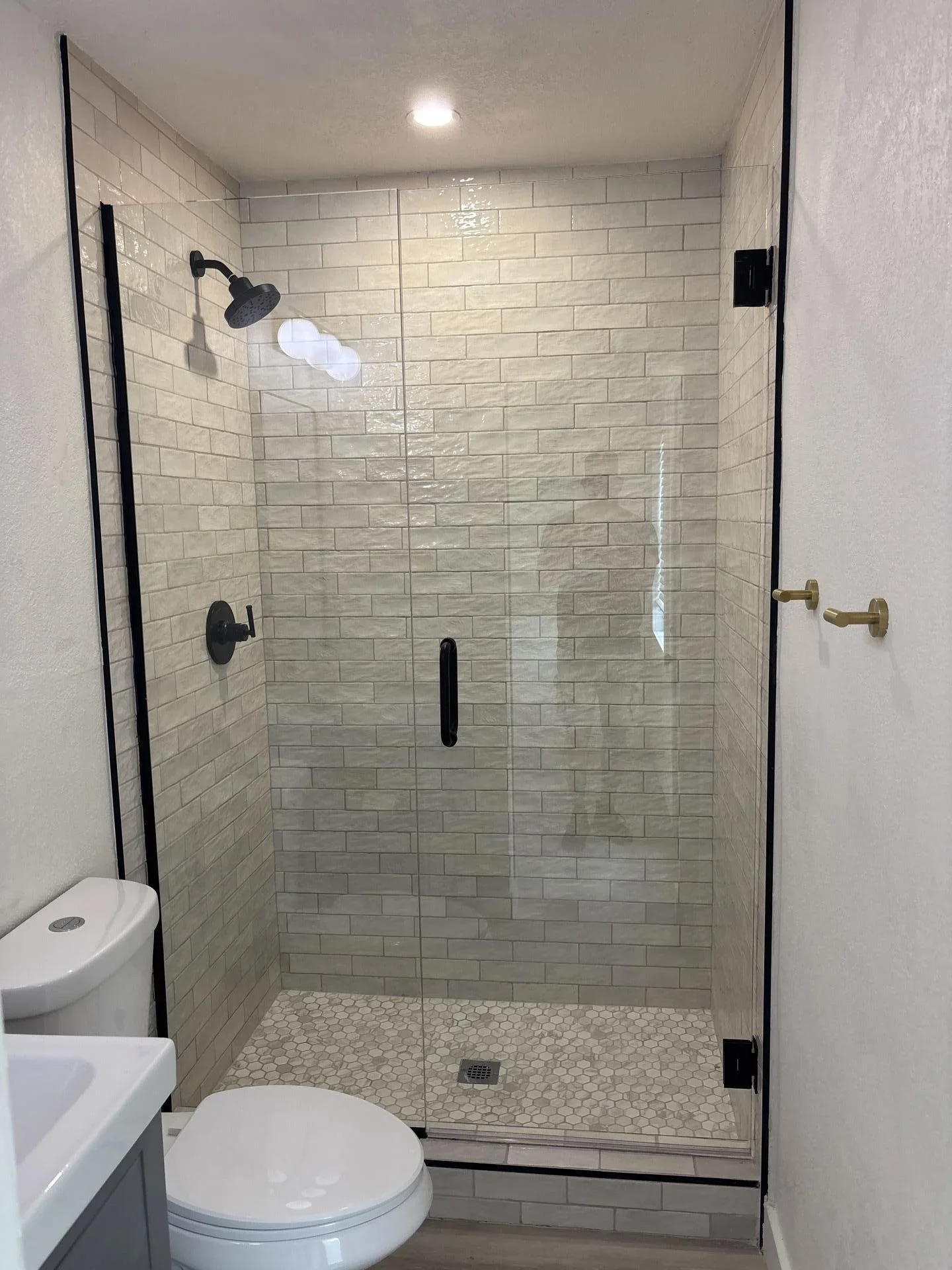 Modern bathroom shower with subway tile walls, hexagonal floor tiles, and frameless glass door