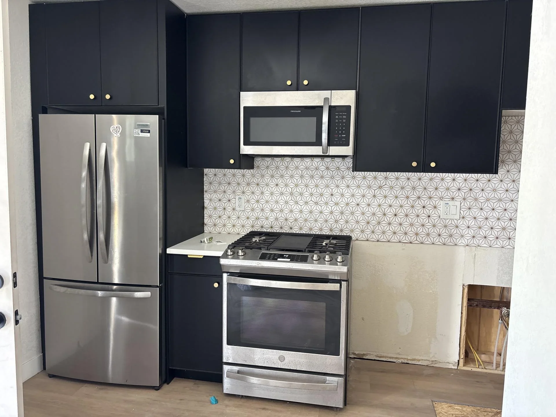 Modern kitchen with dark cabinets, stainless steel appliances, and geometric tile backsplash
